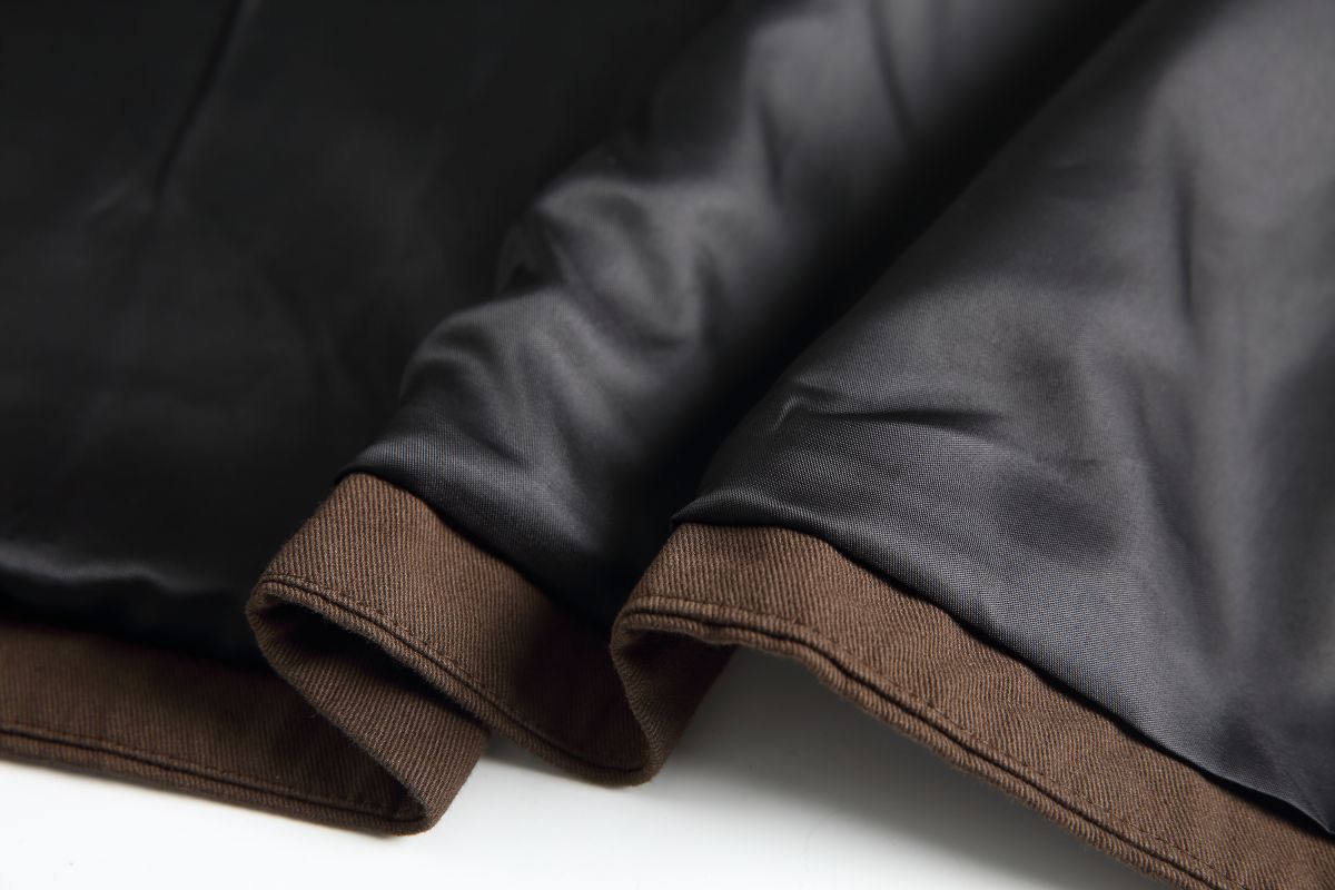 Hem detail of the Hagane jacket showing the brown cotton twill shell against the dark interior lining