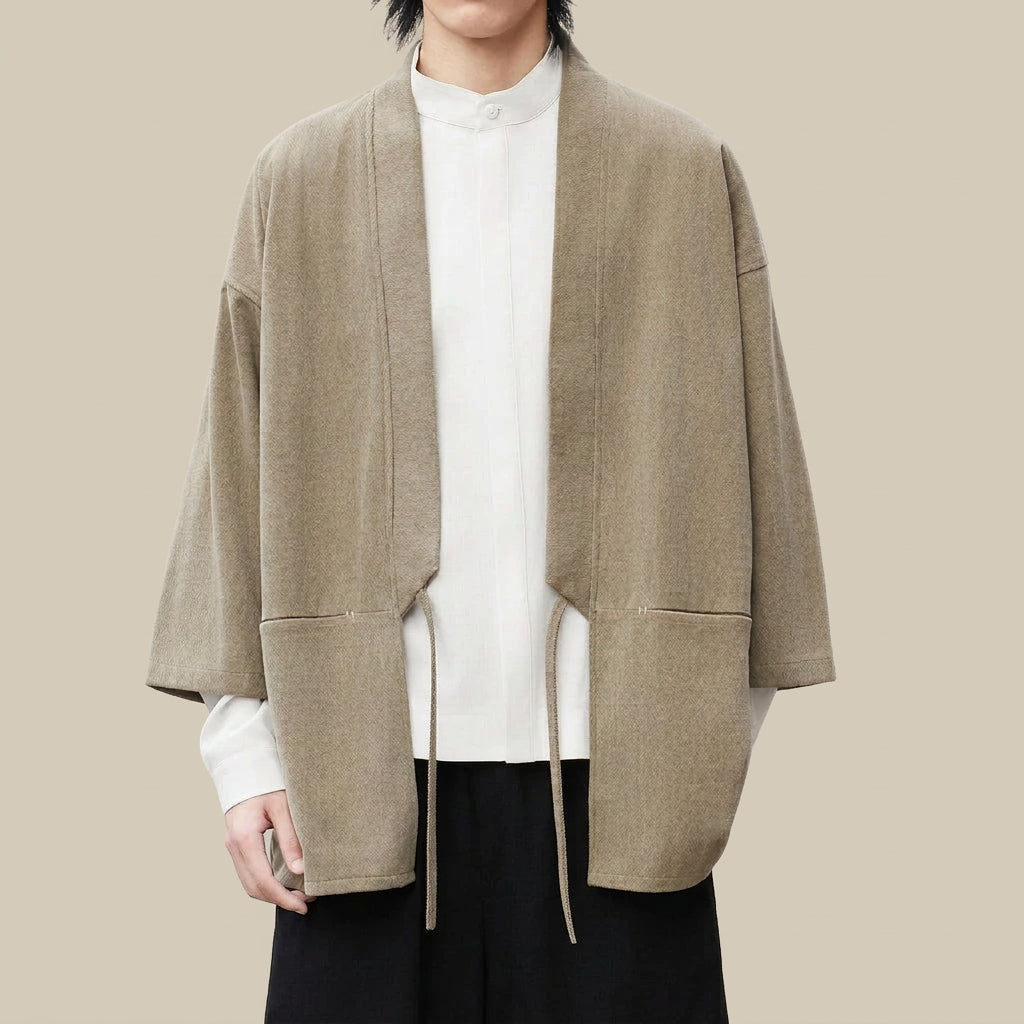 Nagi haori cardigan in beige, worn open over a white stand-collar shirt, showing the wide front bands, hip pockets and waist tie